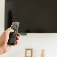 Dłoń trzymająca pilot do telewizora, zastanawiająca się, czy telewizor pobiera dużo prądu.