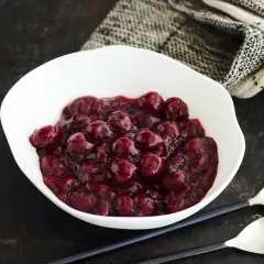 Schüssel mit Kirschsauce, perfekt zum Kirschsauce selber machen. Dazu zwei Löffel und ein gemustertes Tuch.