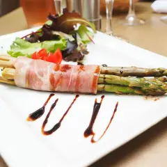 Zielone szparagi owinięte szynką parmeńską, podane z sałatką i sosem balsamicznym.