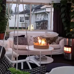 Mysig stuga inredning med soffa, korgstol, växter och tända ljus. En gasolkamin ger värme.