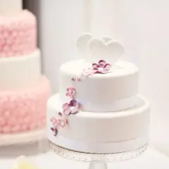 Biały tort dwupiętrowy z sercami i kwiatami, obok różowy tort.