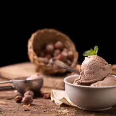 Delizioso gelato alla nocciola appena fatto con la gelatiera, guarnito con menta fresca. Nocciole in un cesto sullo sfondo.