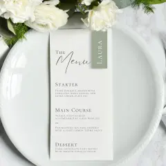 Menu mariage élégant avec des fleurs blanches. La formulation du menu détaille les plats : entrée, plat principal (filet de bœuf ou bar rôti) et dessert.