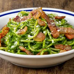 Un piatto invitante di pasta con spinaci e croccante pancetta, cosparso di formaggio grattugiato.