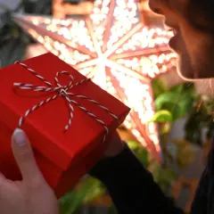 Ein rotes Weihnachtsgeschenk in Händen, im Hintergrund ein leuchtender Stern.
