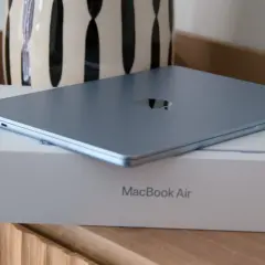 MacBook Air azul cerrado sobre su caja, con un jarrón al fondo.