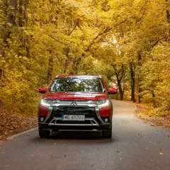 Czerwony Mitsubishi Outlander na jesiennej drodze wśród złotych liści. Sprawdź jego spalanie w podróży!