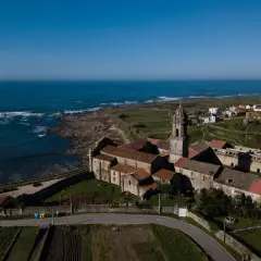 Vista aérea del Monasterio de Santa María de Oia, con el mar azul al fondo y campos verdes.