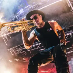 Timmy Trumpet gra na trąbce na scenie w Polsce, otoczony dymem i światłami.