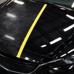 Czarne auto z żółtym pasem dzielącym maskę na część zmatowioną i błyszczącą.