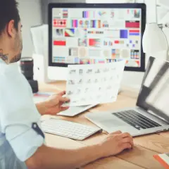 Mężczyzna, jako ux designer, analizuje wydruki przy biurku z komputerem i laptopem.