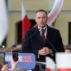 Polityk przemawia na tle flag. Na banerze widnieje napis "NAWROCKI 2025".