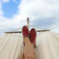 Nogi w czerwonych trampkach odpoczywają na hamaku pod błękitnym niebem. Marzę o tym, ile dni urlopu za przepracowany miesiąc!