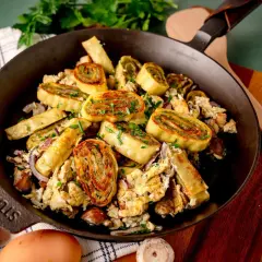 Herzhafte Maultaschen-Pfanne mit Rührei, Zwiebeln und frischen Kräutern, appetitlich in einer Gusseisenpfanne serviert.