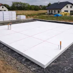 Płyta fundamentowa z białego styropianu, przygotowana do ocieplenia fundamentów. W tle domy w budowie.