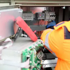Elektryk w pomarańczowej kamizelce pracuje przy panelu sterowania, podłączając kabel neutralny.
