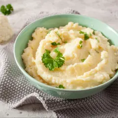 Aksamitne puree z kalafiora, udekorowane natką pietruszki, podane w miętowej miseczce. Obok leżą różyczki kalafiora.