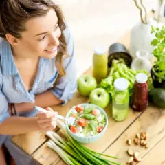Junge Frau isst gesunden Salat. Viele gesunde Lebensmittel wie Obst, Gemüse und Nüsse sind auf dem Tisch, die reich an Cystein sind.