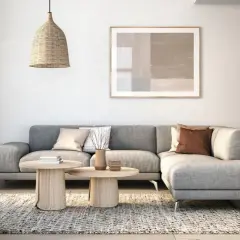 Gemütliches Wohnzimmer mit grauem Sofa, beigefarbenem Sessel, Holztischen und einem Bücherregal. Modernes interior design.