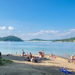 Słoneczny dzień na plaży w Polańczyku-zdroju. Ludzie odpoczywają nad wodą, niektórzy kąpią się, inni opalają.