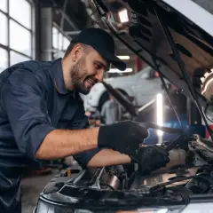 Uśmiechnięty mechanik w granatowym kombinezonie sprawdza silnik. Zastanawiasz się, ile zarabia mechanik?