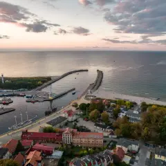 Widok z lotu ptaka na port i plażę w Ustce. Widać liczne łodzie, latarnię morską i falochrony. To idealne miejsce na odkrywanie ustka atrakcje.