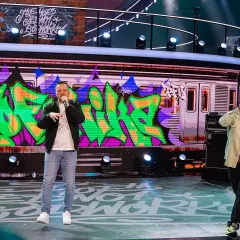 Raperzy na scenie, w tle graffiti na wagonie metra. To scena z koncertu, gdzie brzmią **paktofonika utwory**.