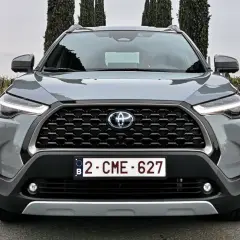 Szary SUV Toyota Hybryda 2022 z przodu, z grillem i światłami LED, na tle winnicy i drzew.