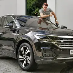 Mężczyzna z kciukiem w górę przy nowym, czarnym Volkswagenie Touareg. Jego imponujące wymiary robią wrażenie.