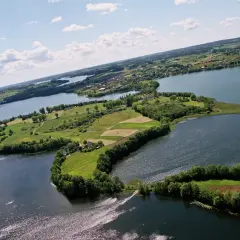 Malowniczy kółko raduńskie z lotu ptaka. Jezioro otacza zielone wyspy z polami i lasami, a w oddali widać zabudowania.