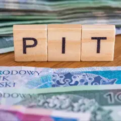 Drewniane klocki z literami "PIT" na tle polskich banknotów. To symbol ulgi na dzieci, która może pomóc w rozliczeniu podatkowym.