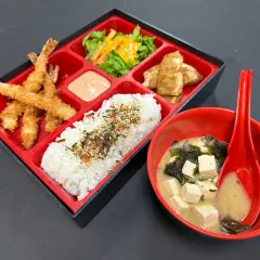 A delicious shrimp bento box with crispy fried shrimp, rice, salad, and tofu, served with miso soup.