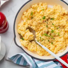 Oeufs brouillés crémeux, parsemés de ciboule fraîche et de poivre noir, servis dans une poêle rouge. Un délice pour le petit-déjeuner.