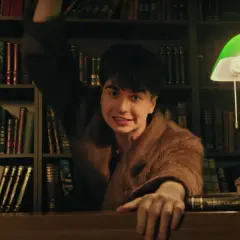 Młody Paderewski w futrze, z ręką uniesioną nad biurkiem, otoczony książkami.