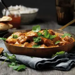 En skål med krämig tikka masala, toppad med färsk koriander, serveras med naanbröd och ris.