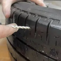 Manos con guantes reparando un pinchazo en un neumático con una herramienta.