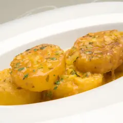 Patatas a la importancia, doradas y jugosas, bañadas en una salsa con ajo y perejil, servidas en un plato blanco.