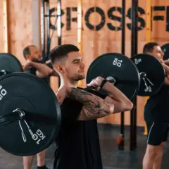 Trzech mężczyzn w siłowni CrossFit wykonuje ćwiczenia ze sztangą na klatce piersiowej.