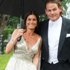 Sian Persson och hennes man, klädda för fest, delar ett paraply i regnet.