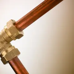 Un coude en laiton relie deux tuyaux en cuivre. Ce raccord per cuivre assure une connexion solide pour la plomberie.