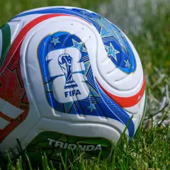 Piłka na mundialu, ozdobiona gwiazdami i logo FIFA, leży na zielonej trawie.