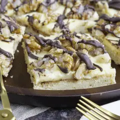 Ein Stück "friss dich dumm Kuchen" mit Walnüssen und Schokoladenglasur auf einem Holzteller, daneben goldenes Besteck.