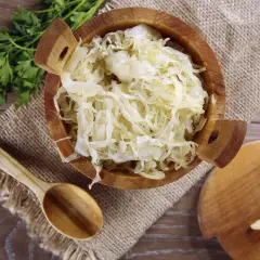 Holzschale mit Sauerkraut, daneben ein Holzlöffel und ein Stück Knoblauch. Manche finden, dass Sauerkraut schmeckt bitter.