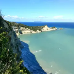 Widok z klifu podczas **Korfu trekking** na turkusowe morze i skaliste wybrzeże.
