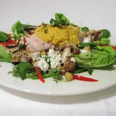 Chicken salad with mushrooms, feta cheese, chickpeas, red pepper, and greens on a white plate.