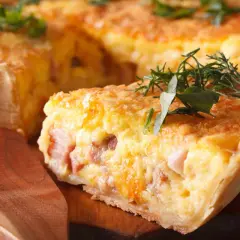 Une part de quiche raclette, garnie d'herbes fraîches, sur une planche en bois. Un délice gourmand !