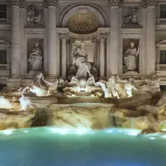 Fontana di Trevi stile barocco, con statue di divinità marine e cavalli marini che emergono da rocce e cascate, illuminata di notte.