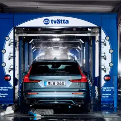 En Volvo är på väg in i en biltvätt. Vatten sprutar och underspolning av bilen pågår.