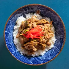 A bowl of fluffy white rice topped with savory pork shogayaki, garnished with bright red pickled ginger.