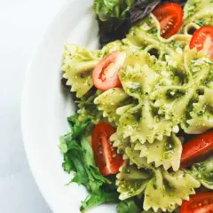 Ein köstlicher italienischer Nudelsalat mit Farfalle, Pesto und Kirschtomaten, garniert mit frischem Salat.